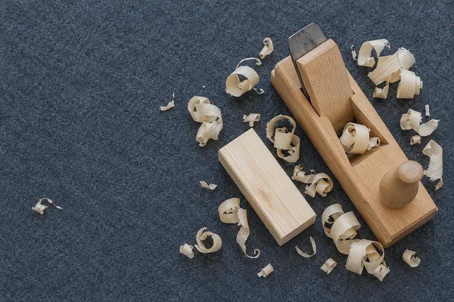 Von oben: Holzhobel aus Buche auf grauem Filz, rundherum helle Hobelspäne und ein Stück gehobeltes Holz